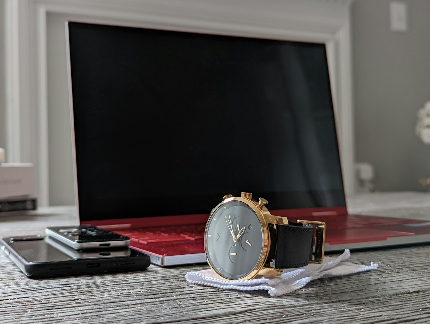 Orologio da polso ed elettronica disposti su una scrivania di legno grigio.
