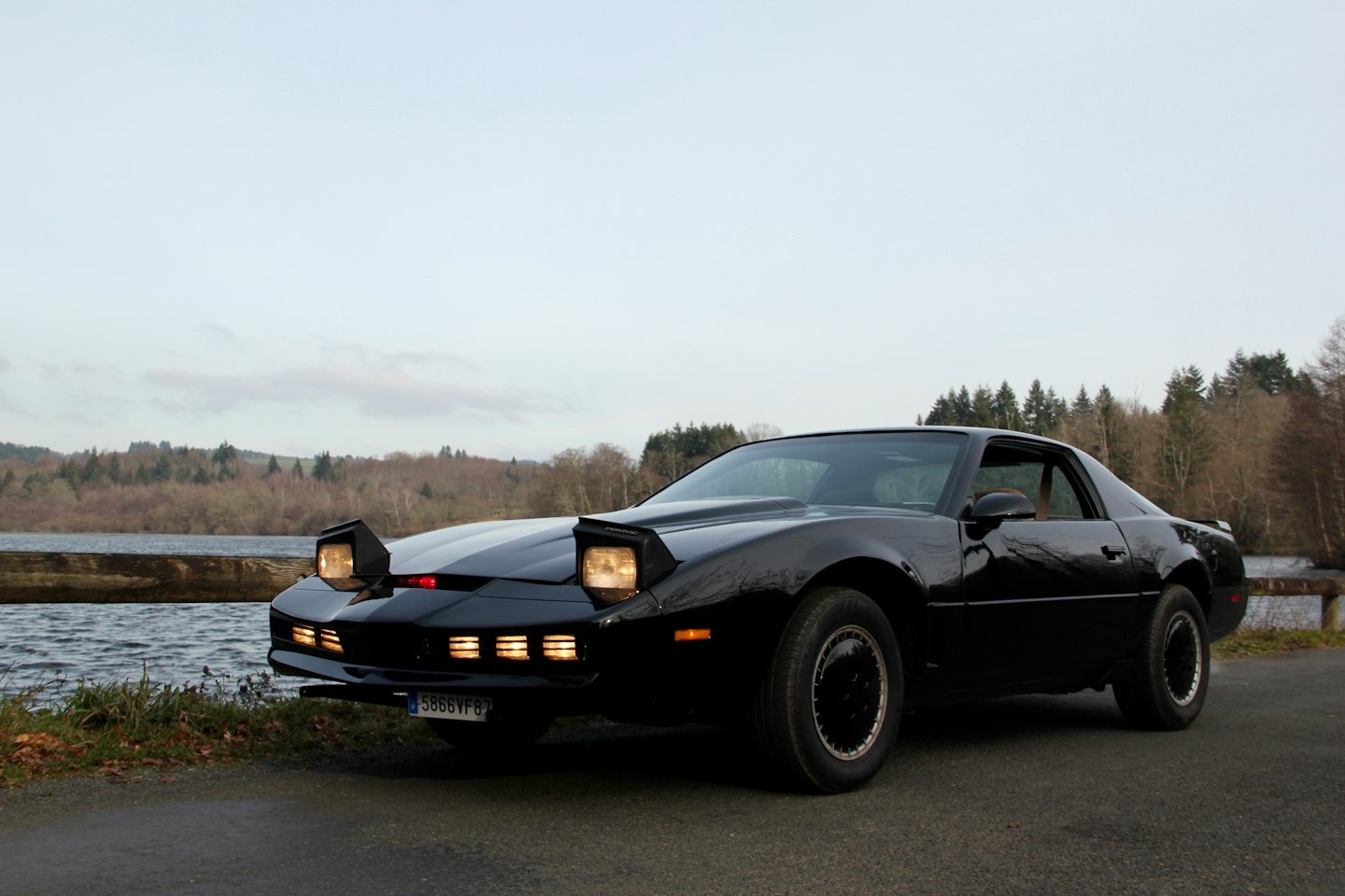 Vettura sportiva d'epoca nera parcheggiata su strada asfaltata vicino a un lago.
