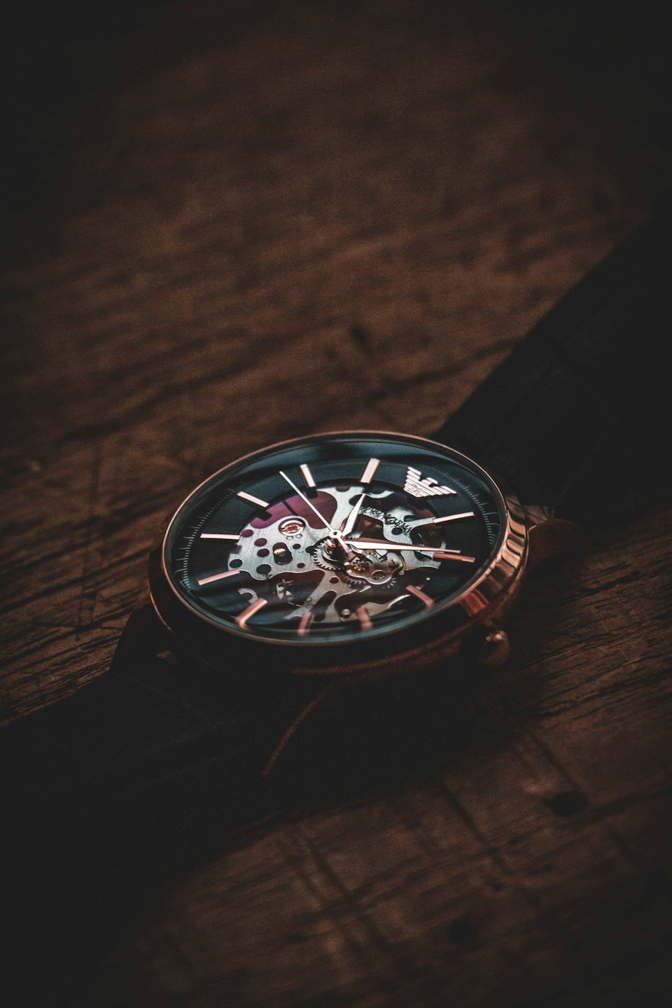 Un orologio da polso scheletrico color oro rosa riposa su una superficie di legno.