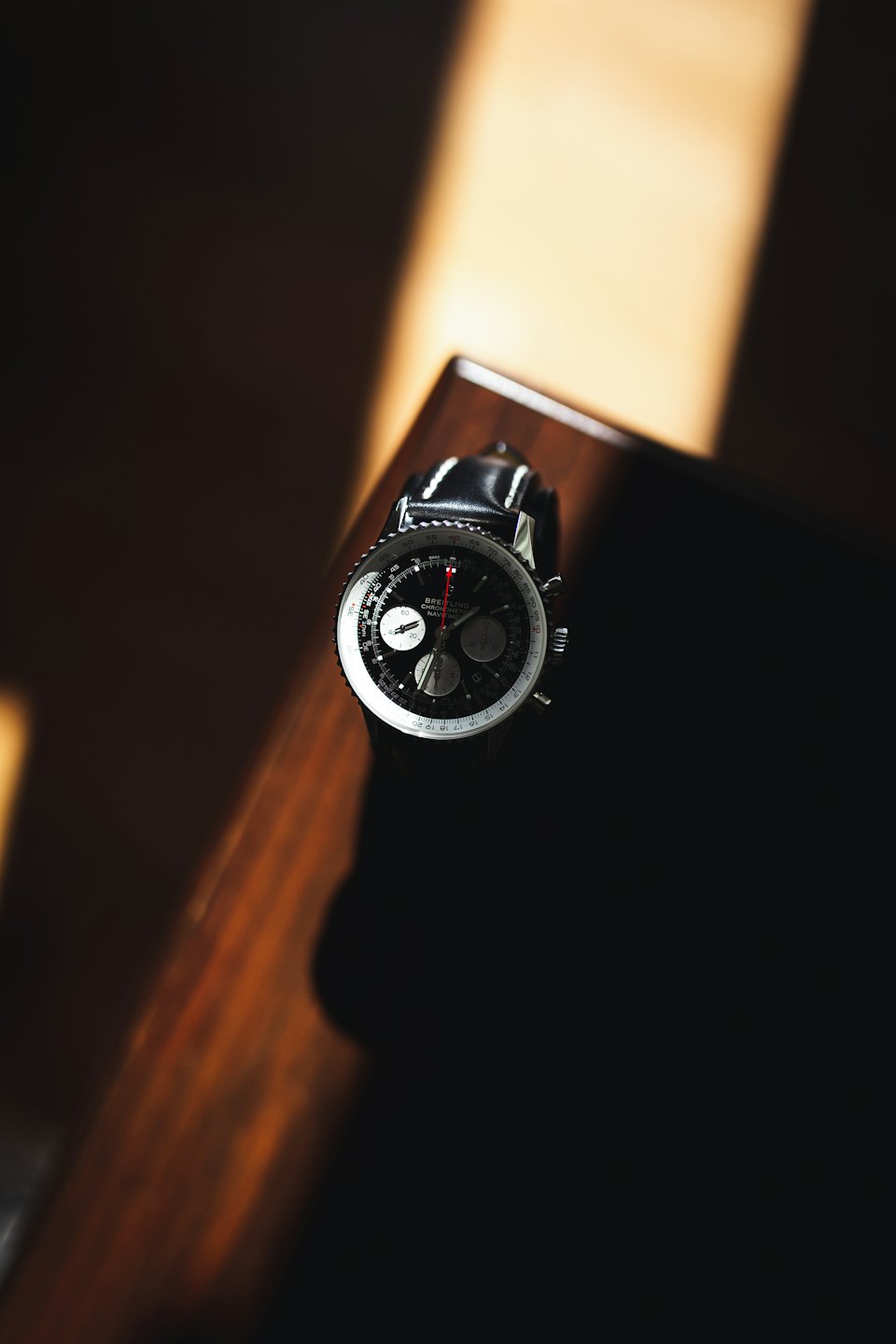 Orologio cronografo d'argento con cinturino in pelle su legno lucido.
