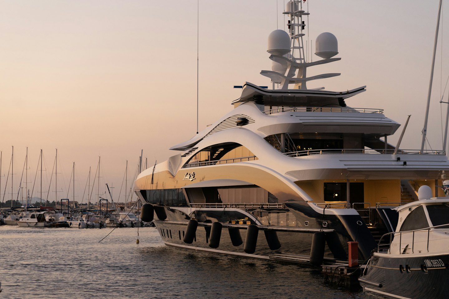 Yacht di lusso ormeggiato in un porto turistico al tramonto con barche a vela.